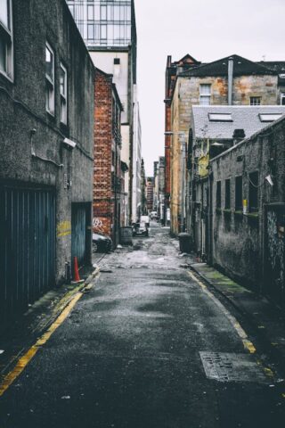 Quiet urban alley with parked cars between old brick buildings, showcasing city life.